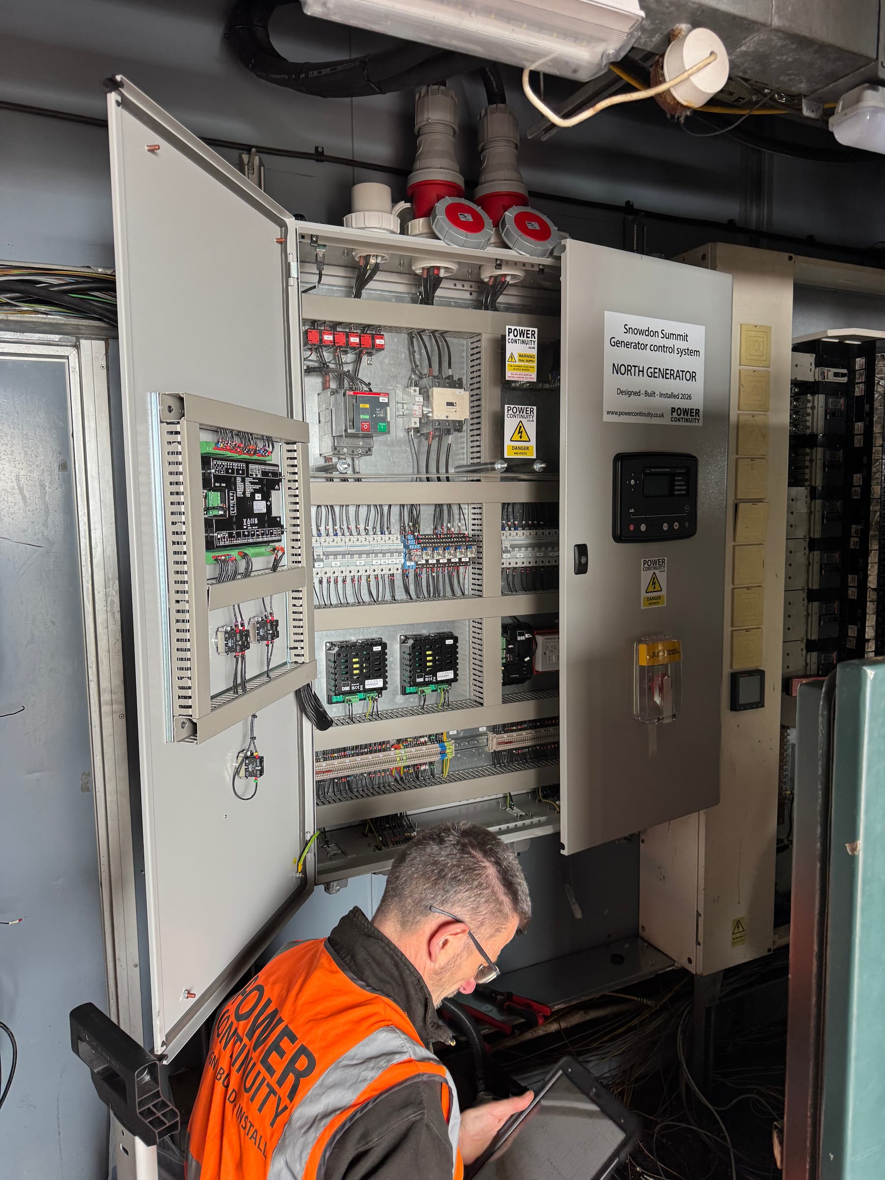 Senior engineer inspecting the open North Generator control panel, custom designed, built, and commissioned in 2026 by Power Continuity.